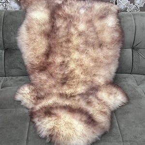 May include: A brown and white sheepskin rug with a long, soft pile. The rug is laid out on a gray couch.