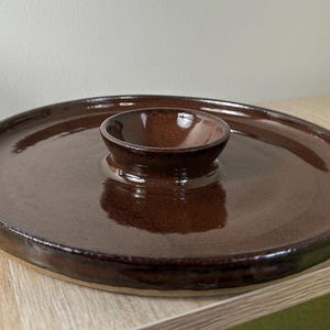 May include: A brown ceramic serving dish with a smaller bowl in the center. The dish has a slightly raised rim and a glossy finish.