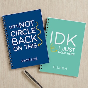 May include: Two spiral-bound notebooks. One is navy blue with the text "LET'S NOT CIRCLE BACK ON THIS" in white, and the name "PATRICE" below. The other is teal with "IDK I JUST WORK HERE" in white, and "EILEEN" below.