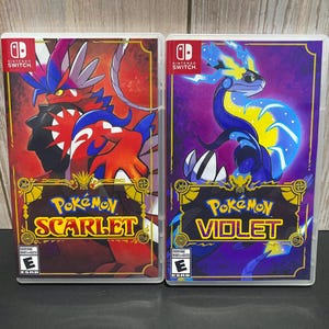 May include: Two Nintendo Switch game cases for Pokemon Scarlet and Pokemon Violet. The Scarlet case features a red and black legendary Pokemon with the text "Pokemon Scarlet" on the front. The Violet case features a blue and purple legendary Pokemon with the text "Pokemon Violet" on the front.