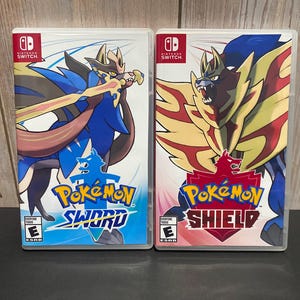 May include: Two Nintendo Switch game cases, one for Pokemon Sword and one for Pokemon Shield. The Sword case features a blue and red Pokemon with a sword, while the Shield case features a red and yellow Pokemon with a shield.