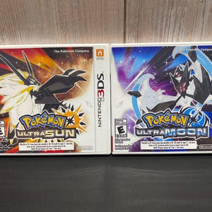 May include: Two Nintendo 3DS game cases for Pokemon Ultra Sun and Pokemon Ultra Moon. The cases are white with blue and red accents. The Pokemon Ultra Sun case features a black and white Pokemon with a yellow and white background. The Pokemon Ultra Moon case features a black and white Pokemon with a blue and white background.