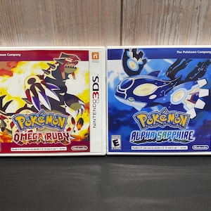 May include: Two Nintendo 3DS game cases, one red and one blue. The red case features the Pokemon Omega Ruby logo and a red and black Pokemon. The blue case features the Pokemon Alpha Sapphire logo and a blue and white Pokemon.