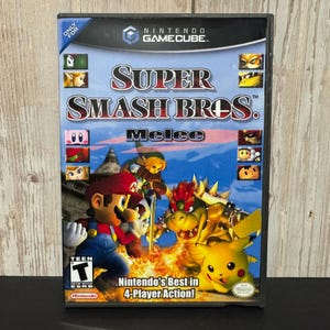 May include: A Nintendo GameCube video game case for Super Smash Bros. Melee. The cover features Mario, Link, Bowser, and Pikachu against a blue sky and fire background. It includes the ESRB Teen rating, the game title, and the text Nintendo's Best in 4-Player Action.