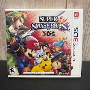 May include: A Super Smash Bros. video game case for the Nintendo 3DS. The cover features various characters from the game, including Mario, Link, and Pikachu. The game is rated Everyone 10+ by the ESRB and is playable in 2D and 3D.