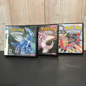 May include: Three Nintendo DS video game cases featuring Pokémon Diamond Version with Dialga, Pokémon Pearl Version with Palkia, and Pokémon Platinum Version with Giratina. Each case displays the game title, the Nintendo DS logo, and the ESRB rating.