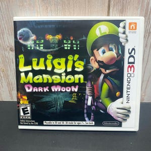 May include: Luigi's Mansion: Dark Moon video game case for the Nintendo 3DS. The cover features Luigi in a green hat, with the game title in yellow and purple. The case is white with the Nintendo 3DS logo.