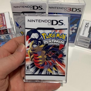 May include: A clear plastic case holds a Nintendo DS game cartridge for Pokemon Platinum Version. The game features a red and black Pokemon with gold accents on a red and white background. The game is rated E for Everyone by the ESRB.