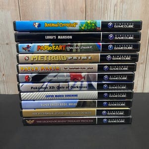 May include: A stack of Nintendo GameCube video game cases. Titles include "Animal Crossing", "Luigi's Mansion", "Mario Kart: Double Dash!!", "Metroid Prime", "Paper Mario: The Thousand-Year Door", "Pokémon Colosseum", "Pokémon XD: Gale of Darkness", "Super Mario Sunshine", "Super Smash Bros. Melee", "The Legend of Zelda: The Wind Waker", and "The Legend of Zelda: Twilight Princess".