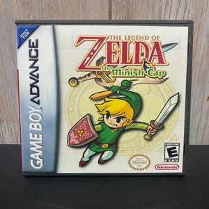 May include: A Game Boy Advance game cartridge case for "The Legend of Zelda: The Minish Cap." The cover art features a cartoon character in a green tunic and hat, holding a sword and shield. The game is rated "E" for Everyone.