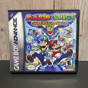 May include: A Game Boy Advance game cartridge for Mario & Luigi: Superstar Saga. The game features a colorful cover with Mario and Luigi on a green path, surrounded by various characters and objects. The game is rated E for Everyone by the ESRB.