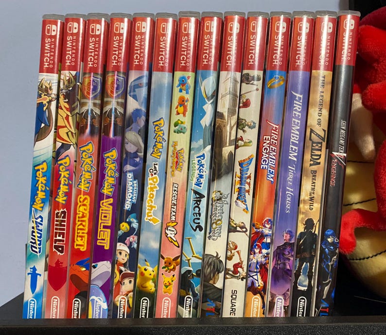 May include: A collection of Nintendo Switch game cases, featuring titles like "Pok&eacute;mon Sword," "Pok&eacute;mon Scarlet," and "The Legend of Zelda: Breath of the Wild." The cases have colorful artwork and the Nintendo Switch logo.