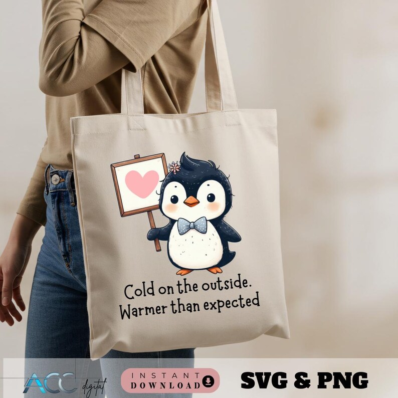 May include: A beige tote bag featuring a cartoon penguin holding a sign with a pink heart. The penguin has a blue bow tie and a flower on its head. Text on the bag reads, "Cold on the outside. Warmer than expected."