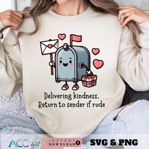 May include: A beige sweatshirt featuring a cartoon mailbox with a smiling face, holding a letter with a heart. The mailbox has a red flag and is surrounded by pink hearts. Text on the shirt reads, "Delivering kindness, Return to sender if rude."
