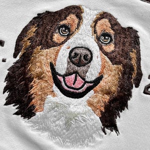 May include: Embroidered image of a dog's face, featuring brown, tan, and white fur. The dog has a happy expression with its tongue visible. The text "EST. 202" is embroidered above and to the right of the dog's face.