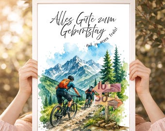 May include: A framed watercolor print featuring two mountain bikers on a dirt trail with snow-capped mountains and pine trees. The text reads "Alles Gute zum Geburtstag" and "Auf zu neuen Trails!" with wooden signs showing 10 and 50 euro banknotes.