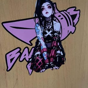 Puede incluir: Una pegatina con un personaje de estilo anime con pelo negro y ojos rojos, vistiendo un top negro y pantalones rojos y negros. El personaje está sobre un gráfico rosa y la palabra "BA" en rosa.