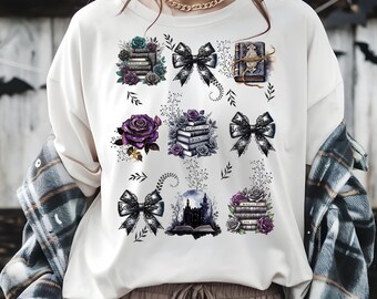 Könnte beinhalten: Cremefarbenes T-Shirt mit gotischen Illustrationen. Das Design umfasst Bücherstapel, Schleifen, Rosen und ein Schloss, alles in Schwarz-, Grau-, Lila- und Türkistönen. Das Shirt hat eine lockere Passform.