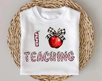 May include: White t-shirt with the text "I TEACHING" in a red and white polka dot design. The letter "I" is a red polka dot apple with a green leaf. A red apple with a black and white checkered bow is also featured.