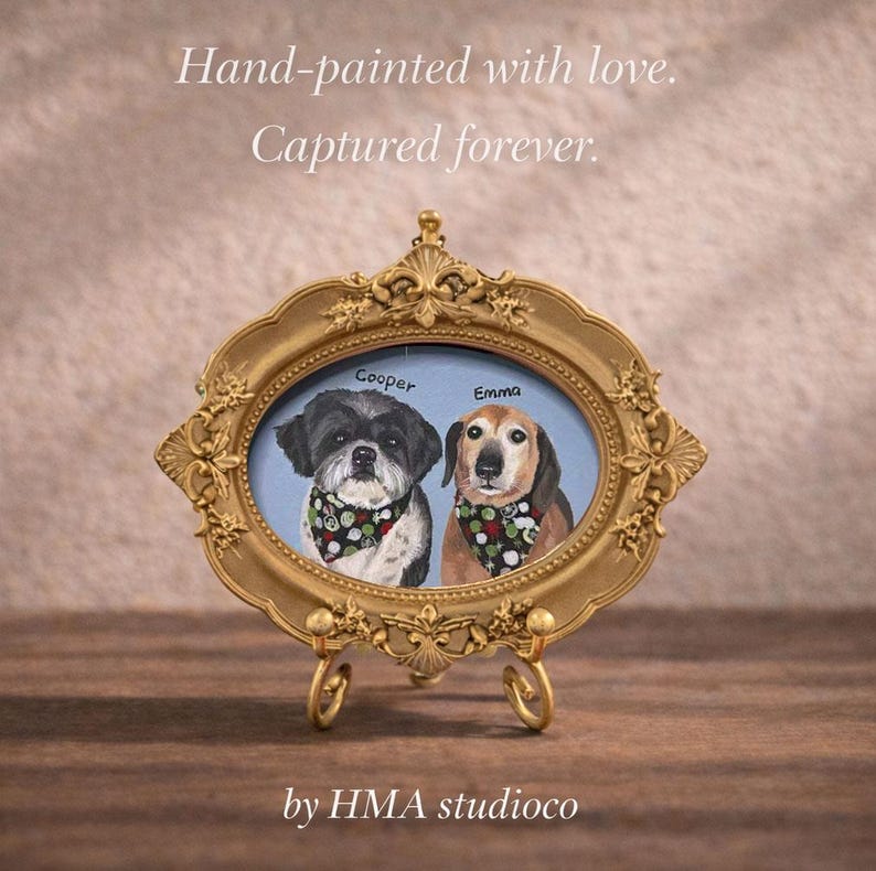 May include: An oval gold-toned ornate frame on a stand containing a painting of two dogs named Cooper and Emma, each wearing a patterned bandana. The text reads: Hand-painted with love. Captured forever. by HMA studioco.