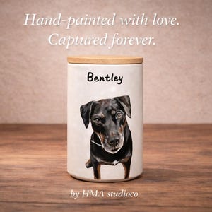May include: A white ceramic canister with a wooden lid featuring a hand-painted portrait of a black dog and the name Bentley printed above it. The text Hand-painted with love. Captured forever. and by HMA studioco are visible in the image.