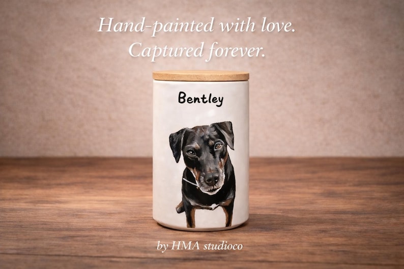 May include: A white ceramic canister with a wooden lid featuring a hand-painted portrait of a black dog and the name Bentley printed above it. The text Hand-painted with love. Captured forever. and by HMA studioco are visible in the image.