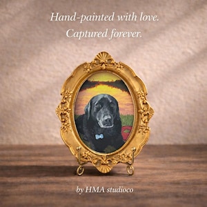 May include: An oval gold-toned ornate picture frame containing a painting of a black Labrador dog wearing a blue collar tag. The text Hand-painted with love. Captured forever. and HMA studioco is visible above and below the framed artwork.