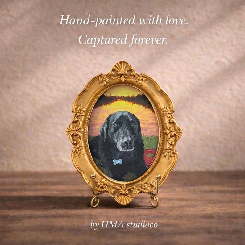 May include: An oval gold-toned ornate picture frame containing a painting of a black Labrador dog wearing a blue collar tag. The text Hand-painted with love. Captured forever. and HMA studioco is visible above and below the framed artwork.