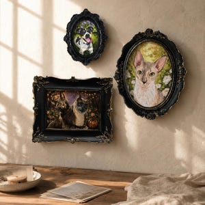 May include: Three ornate black frames with gold accents hang on a wall. One oval frame contains a portrait of a dog, another oval frame features a cat, and a rectangular frame displays two cats with a pumpkin in a dark, festive setting.