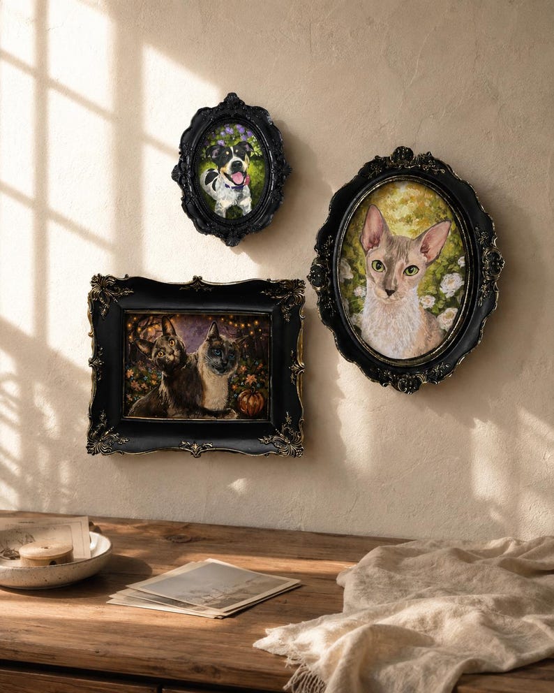 May include: Three ornate black frames with gold accents hang on a wall. One oval frame contains a portrait of a dog, another oval frame features a cat, and a rectangular frame displays two cats with a pumpkin in a dark, festive setting.