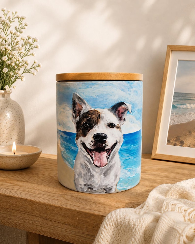 May include: A cylindrical ceramic canister featuring a hand-painted portrait of a smiling dog with white and brown fur. The background depicts a beach scene with blue ocean waves and sandy shores. The container is topped with a round, light wood lid.