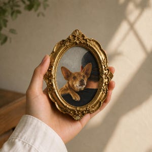 May include: An oval-shaped, ornate gold-colored picture frame featuring intricate floral and scrollwork detailing. The frame contains a portrait of a brown dog with large ears resting its head on a person's shoulder, who is wearing a dark shirt.