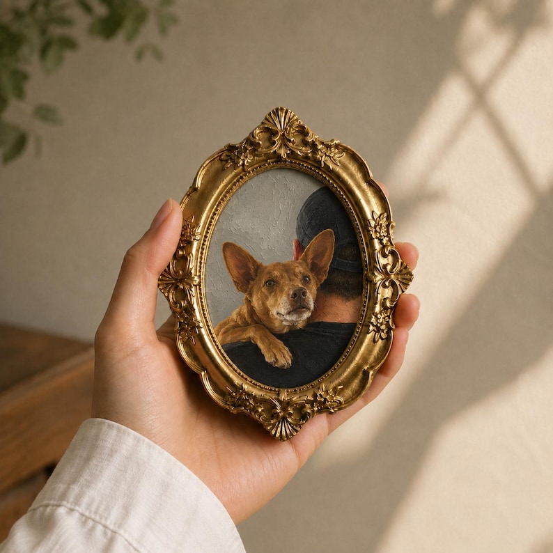 May include: An oval-shaped, ornate gold-colored picture frame featuring intricate floral and scrollwork detailing. The frame contains a portrait of a brown dog with large ears resting its head on a person's shoulder, who is wearing a dark shirt.