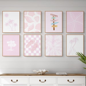 May include: A set of nine pink and white framed prints with beach-themed designs, including palm trees, seashells, flip-flops, and a sign that says "Turn Left to Beach". The prints are arranged in a grid pattern on a white wall above a white dresser with three drawers.