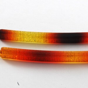 May include: Two amber and brown plastic hair clips with a metal clasp. The clips are graduated in color from yellow to brown.