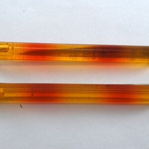 May include: Two amber and orange colored glass rods with a metal tip on each end. The rods are approximately 4 inches long.