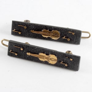 May include: Two black hair clips with gold musical notes and a violin design.
