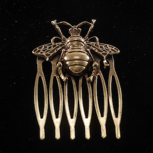 Puede incluir: Peine de pelo de abeja dorada con un diseño de abeja detallado y siete dientes. El peine está hecho de metal y tiene un acabado brillante.