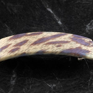 May include: A white and purple patterned hair clip. The clip is made of plastic and has a curved shape.