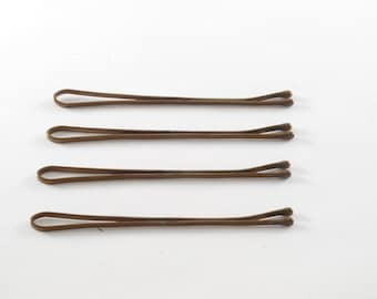 Puede incluir: Cuatro horquillas marrones, también conocidas como horquillas para el cabello, están dispuestas en fila sobre un fondo blanco.
