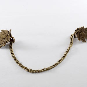 May include: A gold chain with two leaf-shaped clasps. The chain is connected to the clasps, which are in the shape of leaves.