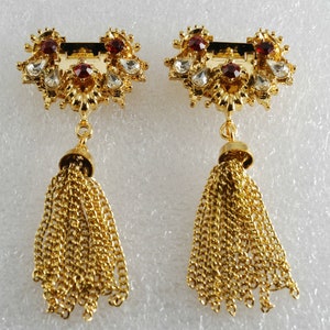 May include: A pair of gold tone earrings with red and clear rhinestones and gold chain tassels.