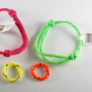 Könnte beinhalten: Drei bunte Freundschaftsarmbänder aus geflochtenem Seil. Ein Armband ist pink mit blauen Streifen, ein anderes ist grün mit gelben Streifen und die letzten beiden sind kleinere Ringe, einer gelb mit orangefarbenen Streifen und der andere orange mit gelben Streifen.
