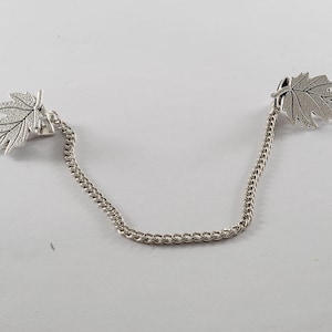 May include: A silver chain with two leaf-shaped charms. The leaves are detailed with a textured surface.