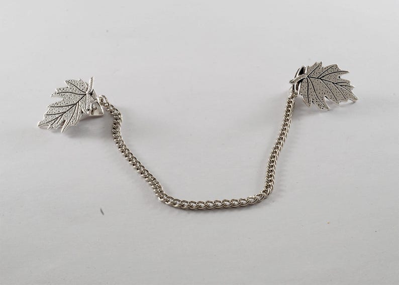 May include: A silver chain with two leaf-shaped charms. The leaves are detailed with a textured surface.