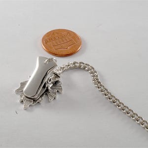 May include: Silver tone chain with a clip and a decorative leaf design. The chain is about the size of a US penny.