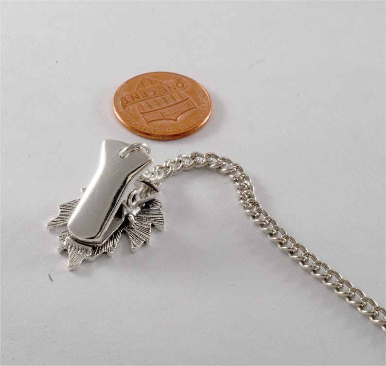 May include: Silver tone chain with a clip and a decorative leaf design. The chain is about the size of a US penny.