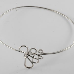 May include: A silver bangle bracelet with a delicate, interwoven knot design.