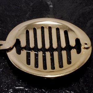 May include: Gold-toned metal hair clip with a rounded shape and a grid of vertical bars. The clip has a hinged design.