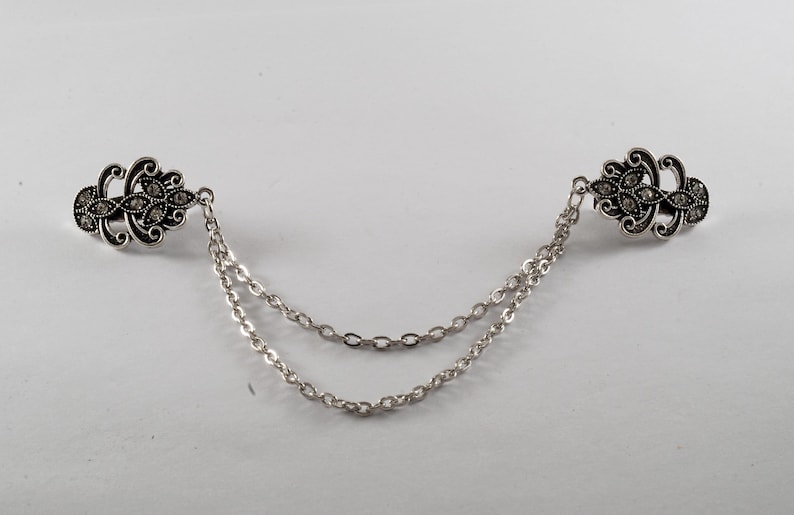 Puede incluir: Una cadena de plata con dos cierres ornamentales de plata en forma de flor. Los cierres est&aacute;n decorados con peque&ntilde;os diamantes de imitaci&oacute;n transparentes.